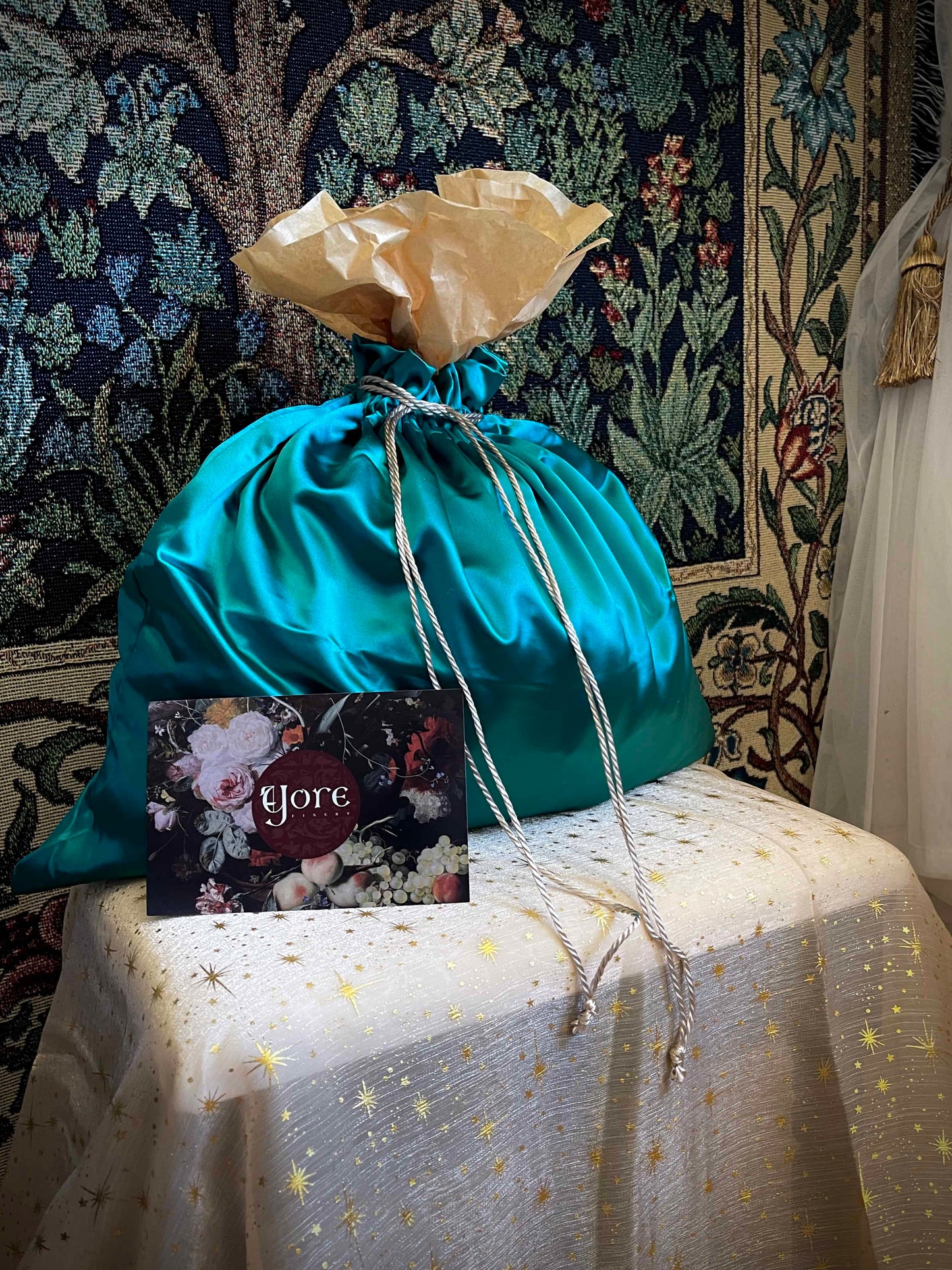 A historical fashion style bundle mystery bag in a satin drawstring bag sits on a celestial puff in front of a historically inspired tapestry.