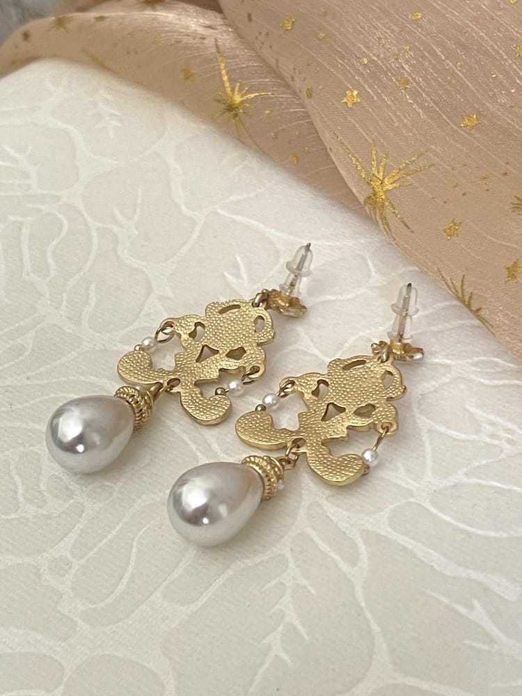 A pair of gold-colored Renaissance Inspired Ornate Flourish Earrings with Pearl Drops, pictured on a floral puff. Silver plated pins.