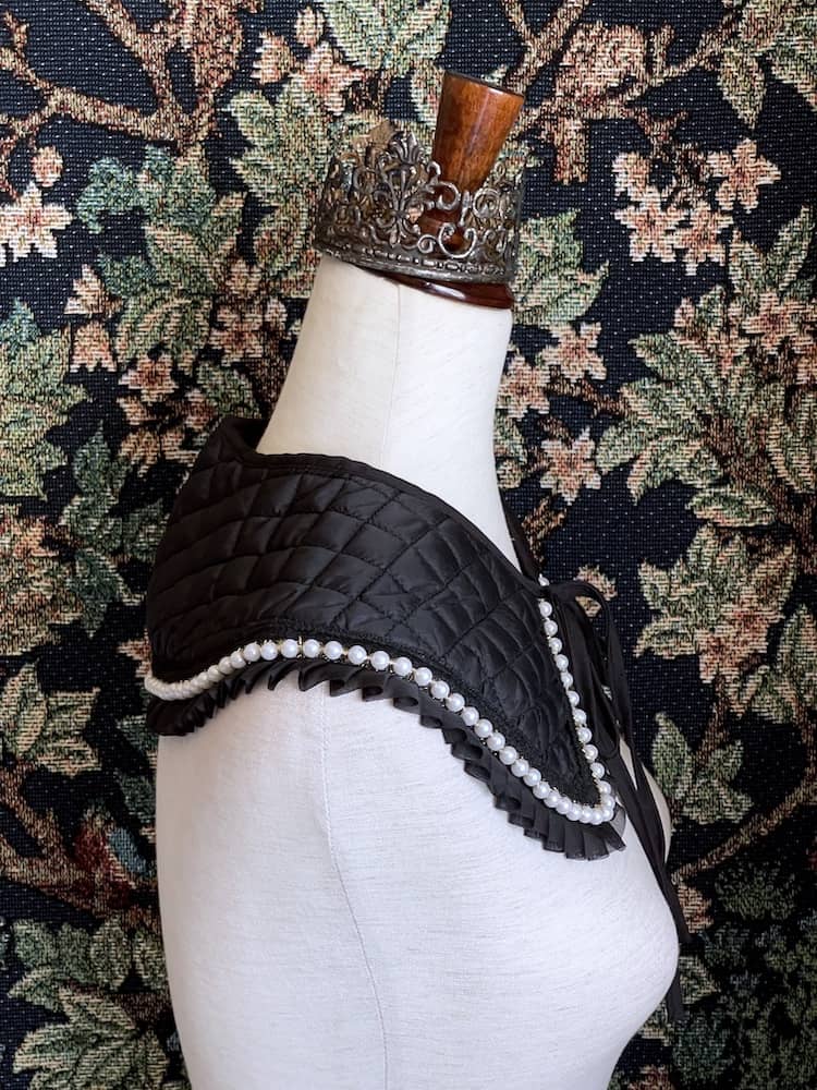 A Historically Inspired Quilted Round Collar with Ruffle & Pearl Trim in Black pictured on a mannequin.