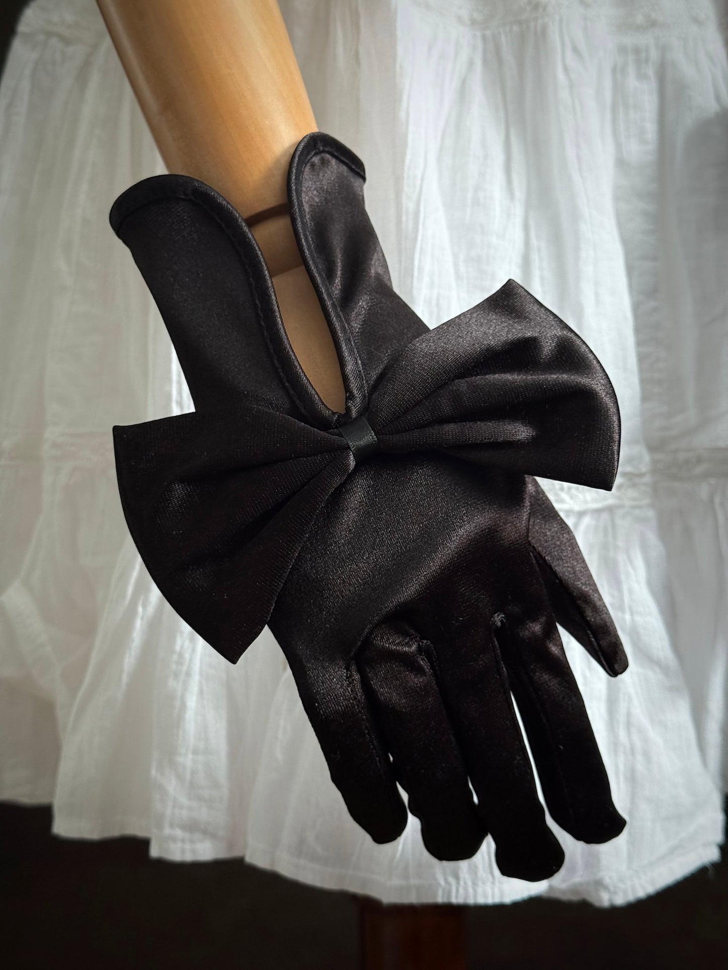 A pair of historically inspired Regency & Victorian era Satin Gloves with Large Bow Detail in Black, pictured on a mannequin in front of an art historical backdrop.