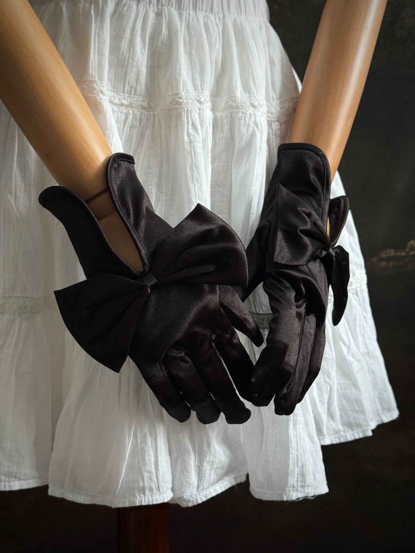 A pair of historically inspired Regency & Victorian era Satin Gloves with Large Bow Detail in Black, pictured on a mannequin in front of an art historical backdrop.