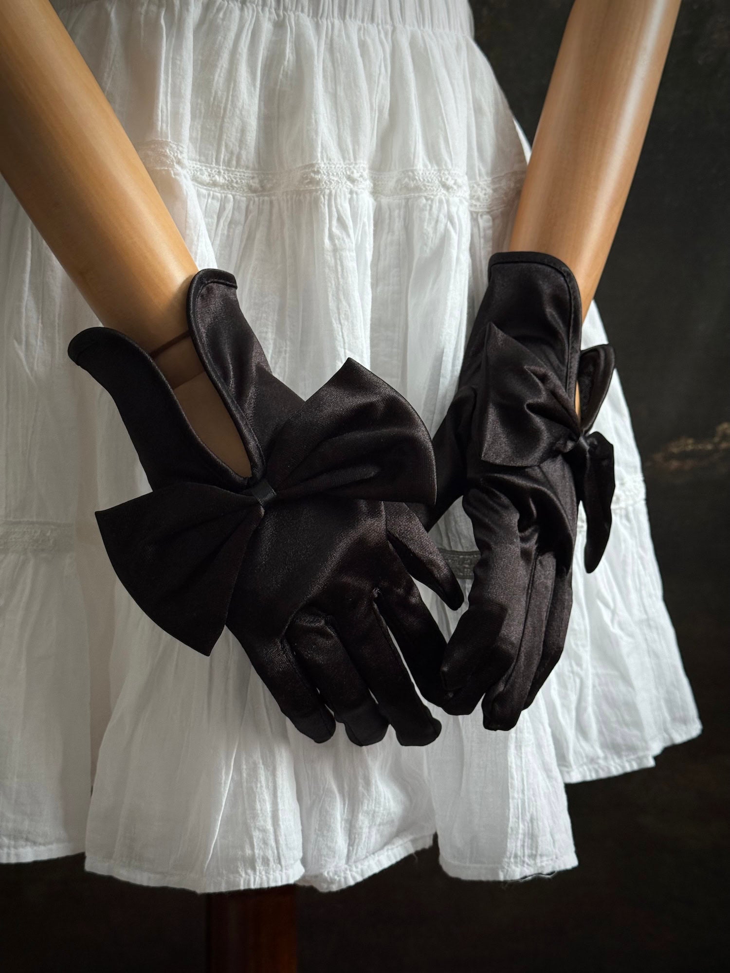 A pair of historically inspired Regency & Victorian era Satin Gloves with Large Bow Detail in Black, pictured on a mannequin in front of an art historical backdrop.