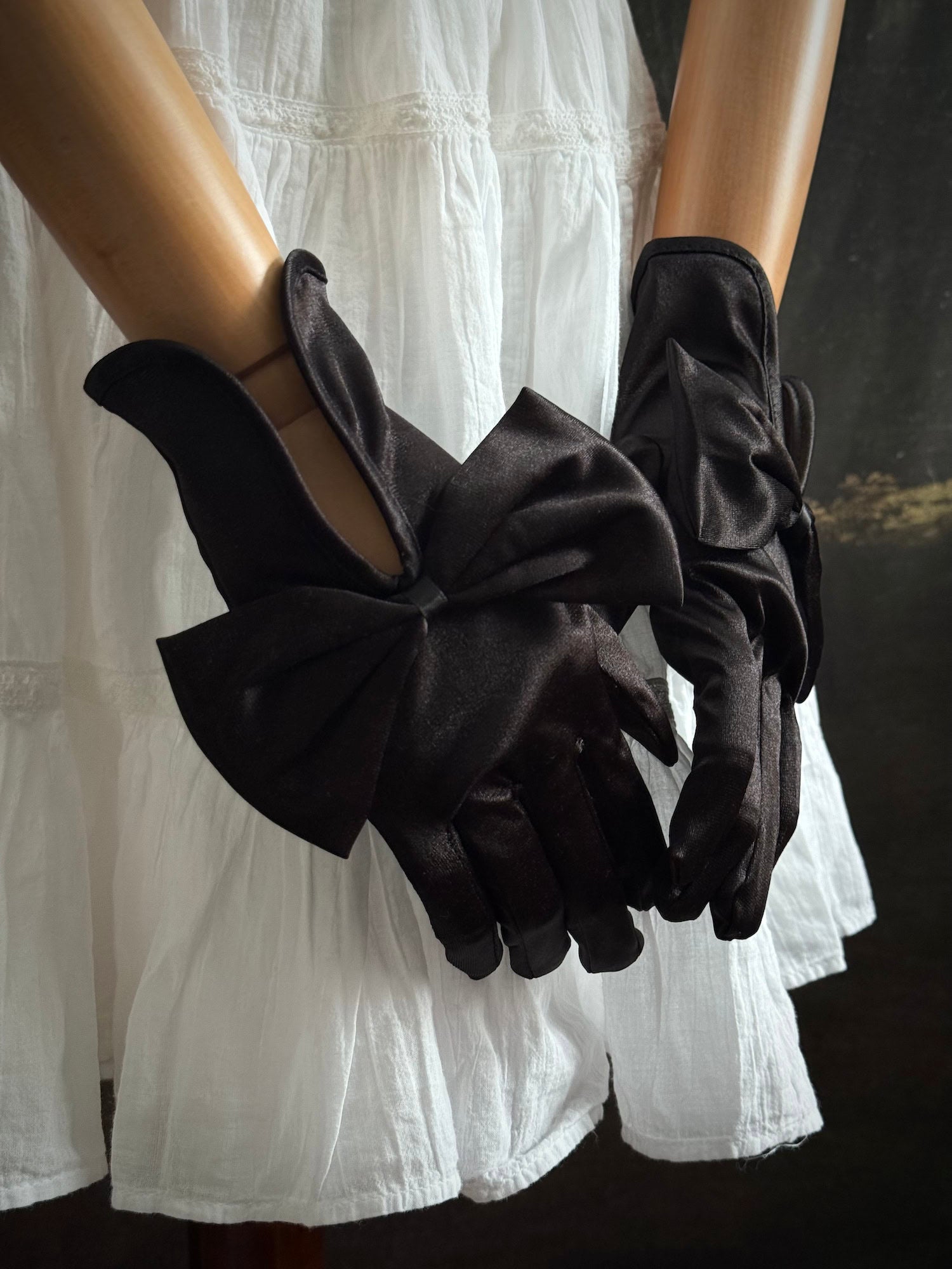 A pair of historically inspired Regency & Victorian era Satin Gloves with Large Bow Detail in Black, pictured on a mannequin in front of an art historical backdrop.