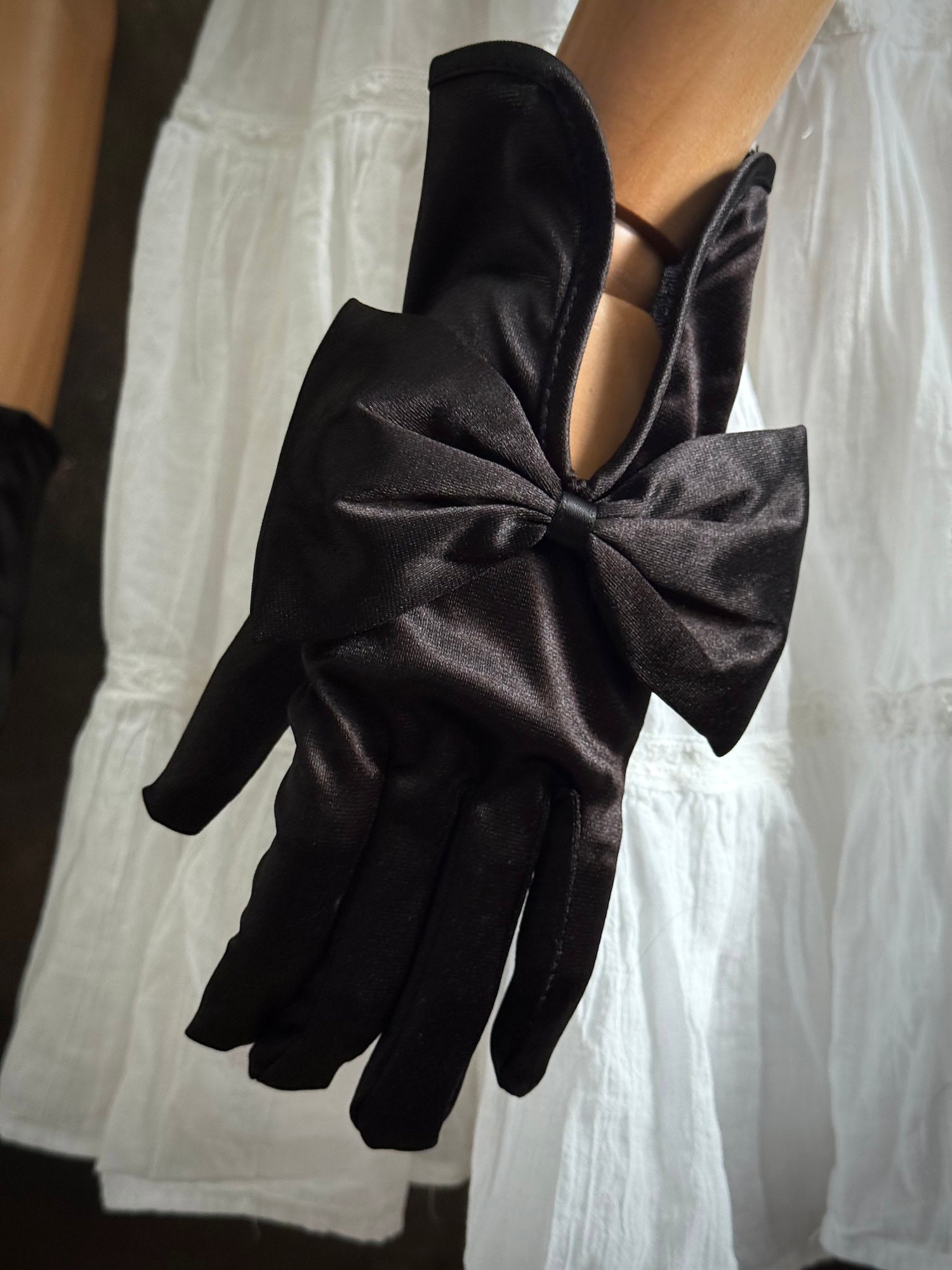 A pair of historically inspired Regency & Victorian era Satin Gloves with Large Bow Detail in Black, pictured on a mannequin in front of an art historical backdrop.