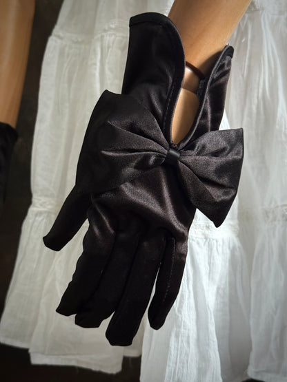 A pair of historically inspired Regency & Victorian era Satin Gloves with Large Bow Detail in Black, pictured on a mannequin in front of an art historical backdrop.