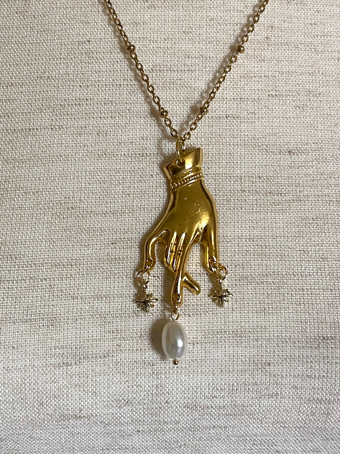 A Handmade Historically Inspired Medieval Hand Pendant Necklace with Real Baroque Pearl Dangle and Celestial Star Charms on a Metal Beaded Chain Necklace in Gold.