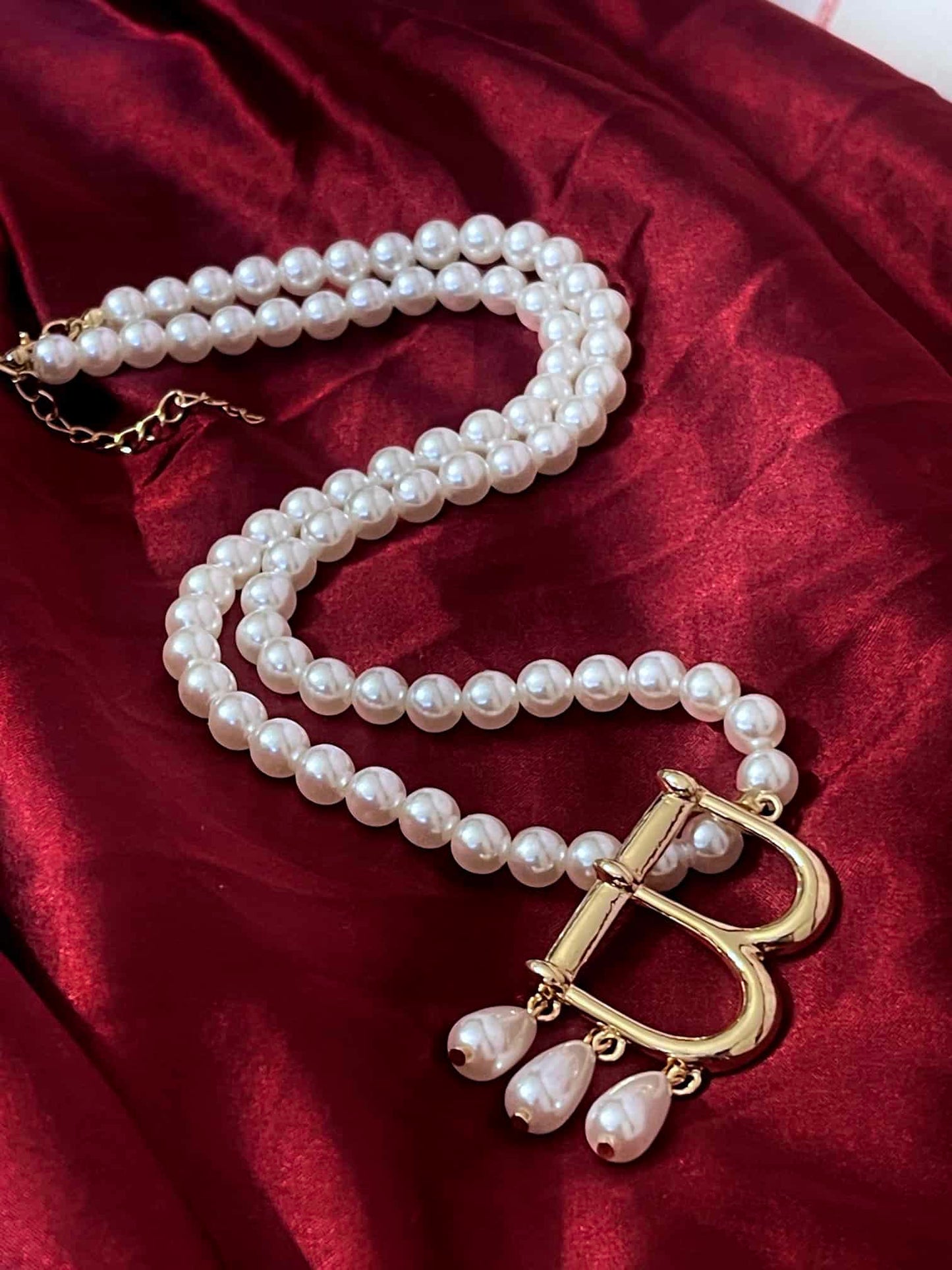 A Historical Tudor Fashion Inspired Anne Boleyn "B" Pearl Necklace on a mannequin in front of an ornate backdrop. 