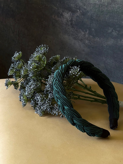 A historically inspired vintage style braided headband in dark forest green is pictured with a floral bouquet in front of an art history backdrop.