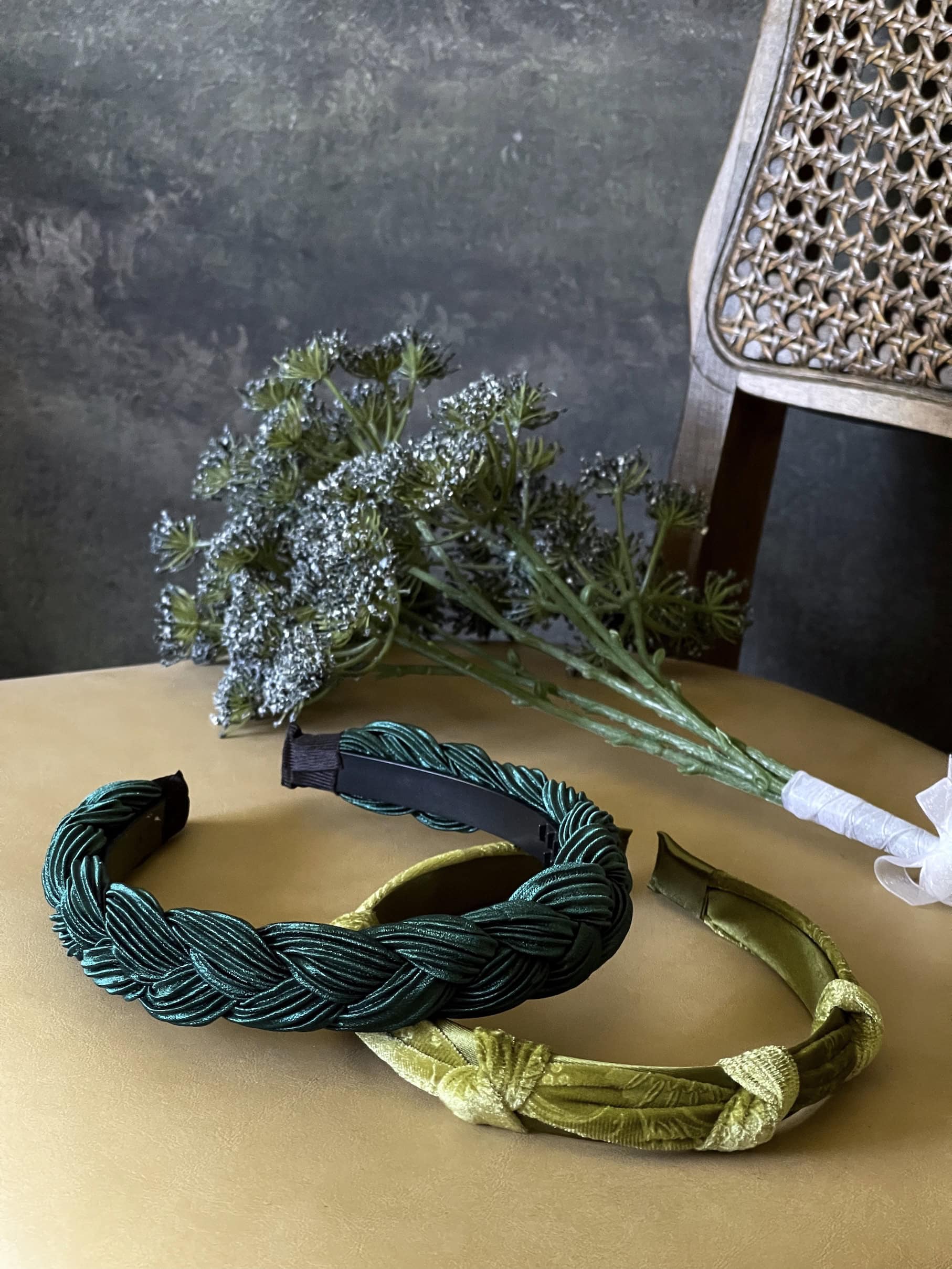 A historically inspired vintage style velvet floral knotted headband in mossy olive green is pictured with a bouquet in front of an art history backdrop.
