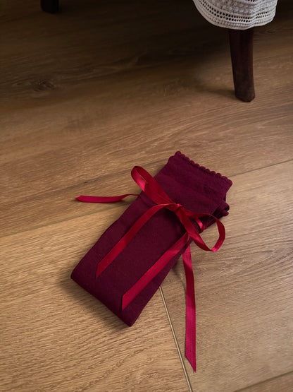 A pair of Historically Inspired Cotton Knee-High Socks with Satin Ribbon Lacing in a dark Burgundy red, pictured on a wooden cottage floor.