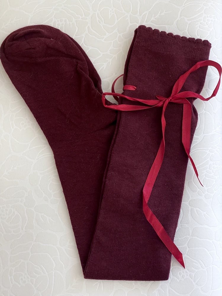 A pair of Historically Inspired Cotton Knee-High Socks with Ribbon Lacing in Burgundy, on a puff. Stockings for any historical era.