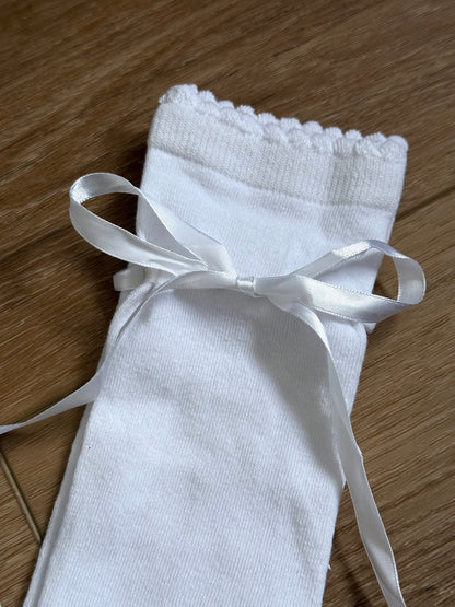 A pair of Historically Inspired Cotton Knee-High Socks with Satin Ribbon Lacing in bright White, pictured on a historic wooden cottage floor.