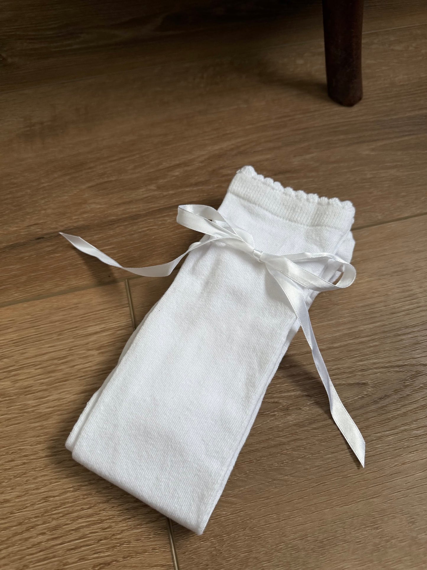A pair of Historically Inspired Cotton Knee-High Socks with Satin Ribbon Lacing in bright White, pictured on a historic wooden cottage floor.