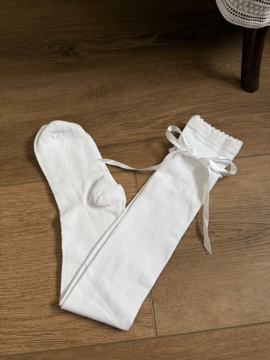 A pair of Historically Inspired Cotton Knee-High Socks with Satin Ribbon Lacing in bright White, pictured on a historic wooden cottage floor.