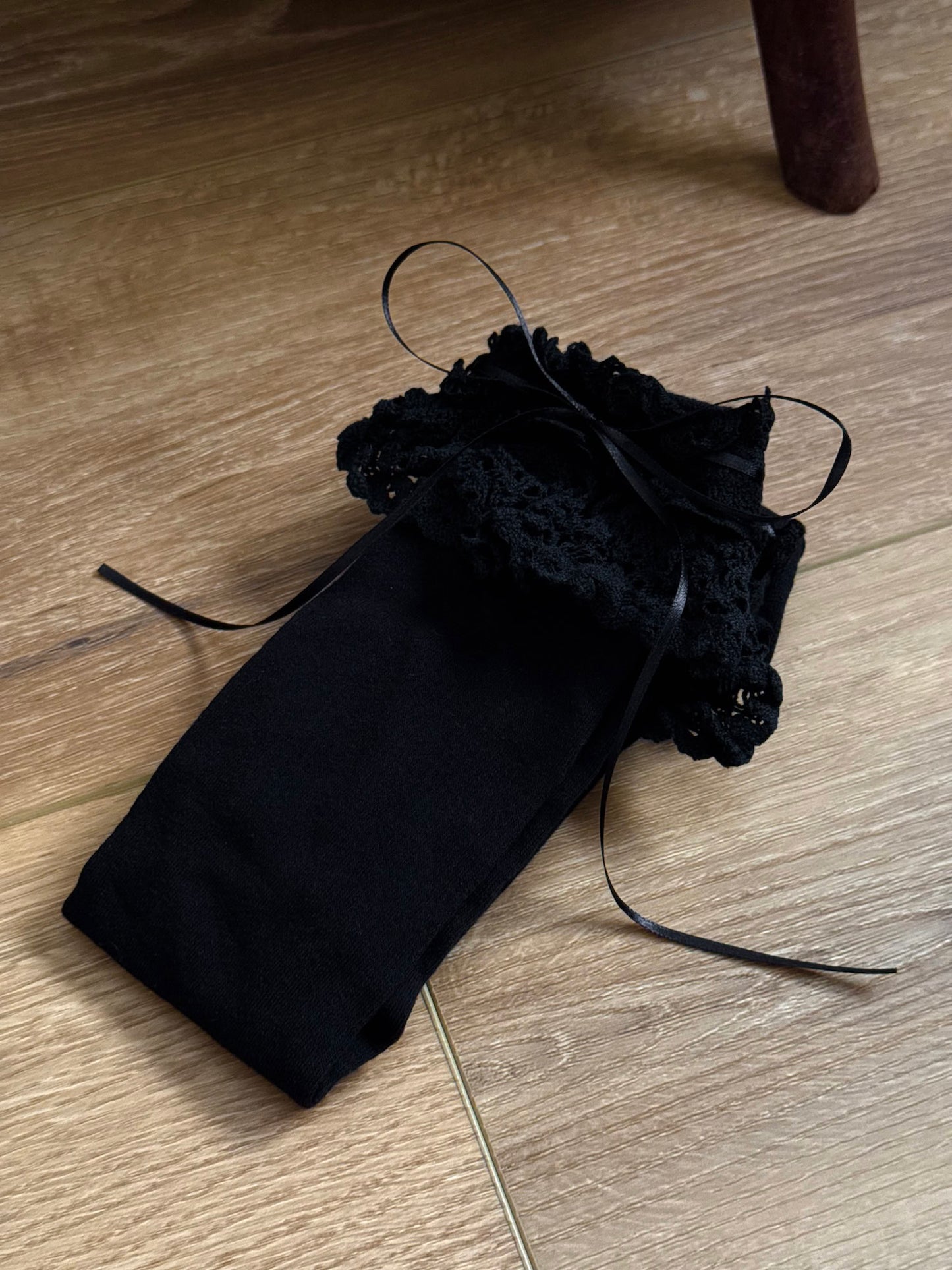 Historically Inspired Cotton Knee-High Socks with ruffled Lace Trim and ribbon ties in gothic Black on a cottagecore wooden floor.