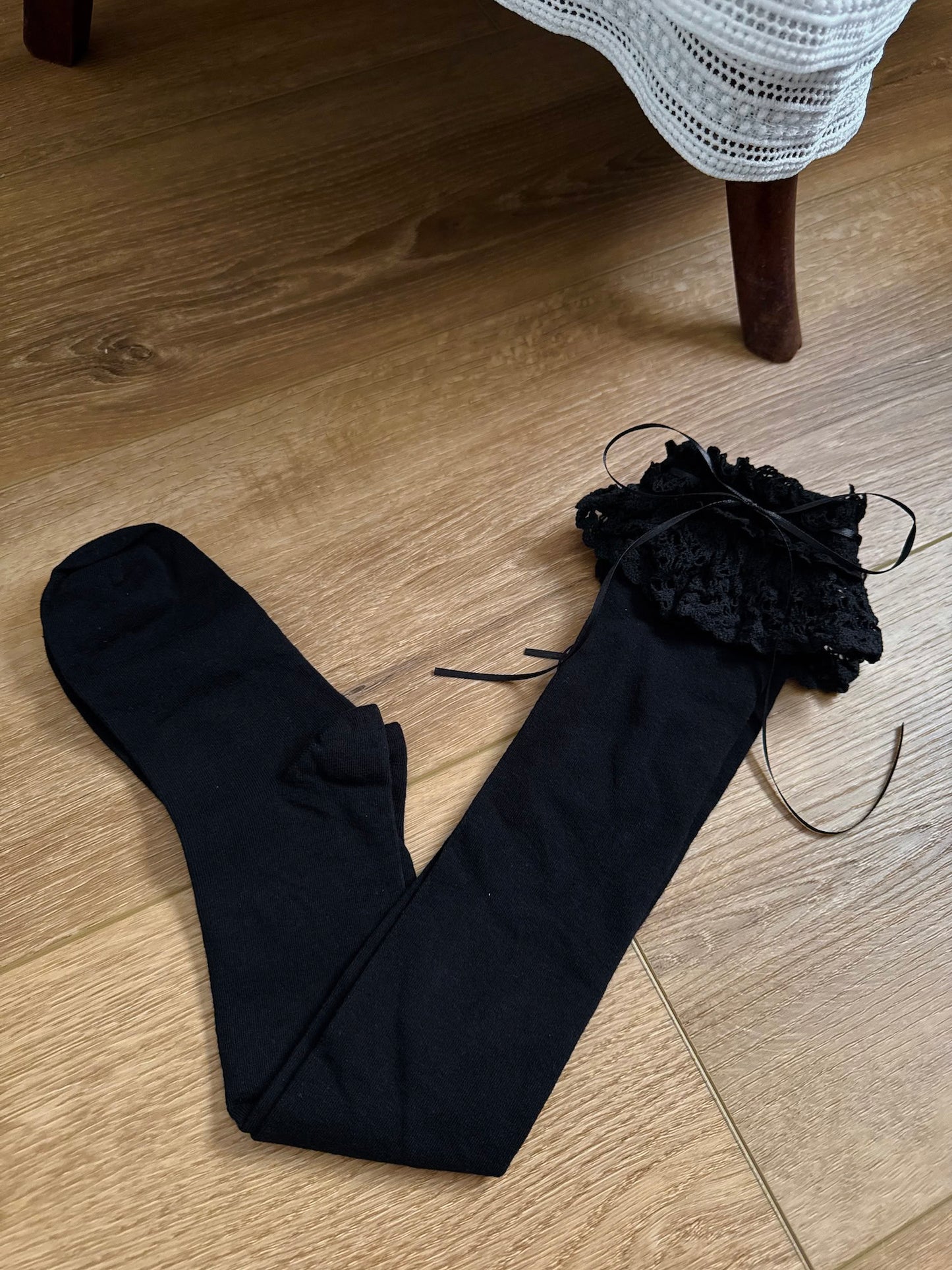 Historically Inspired Cotton Knee-High Socks with ruffled Lace Trim and ribbon ties in gothic Black on a cottagecore wooden floor.