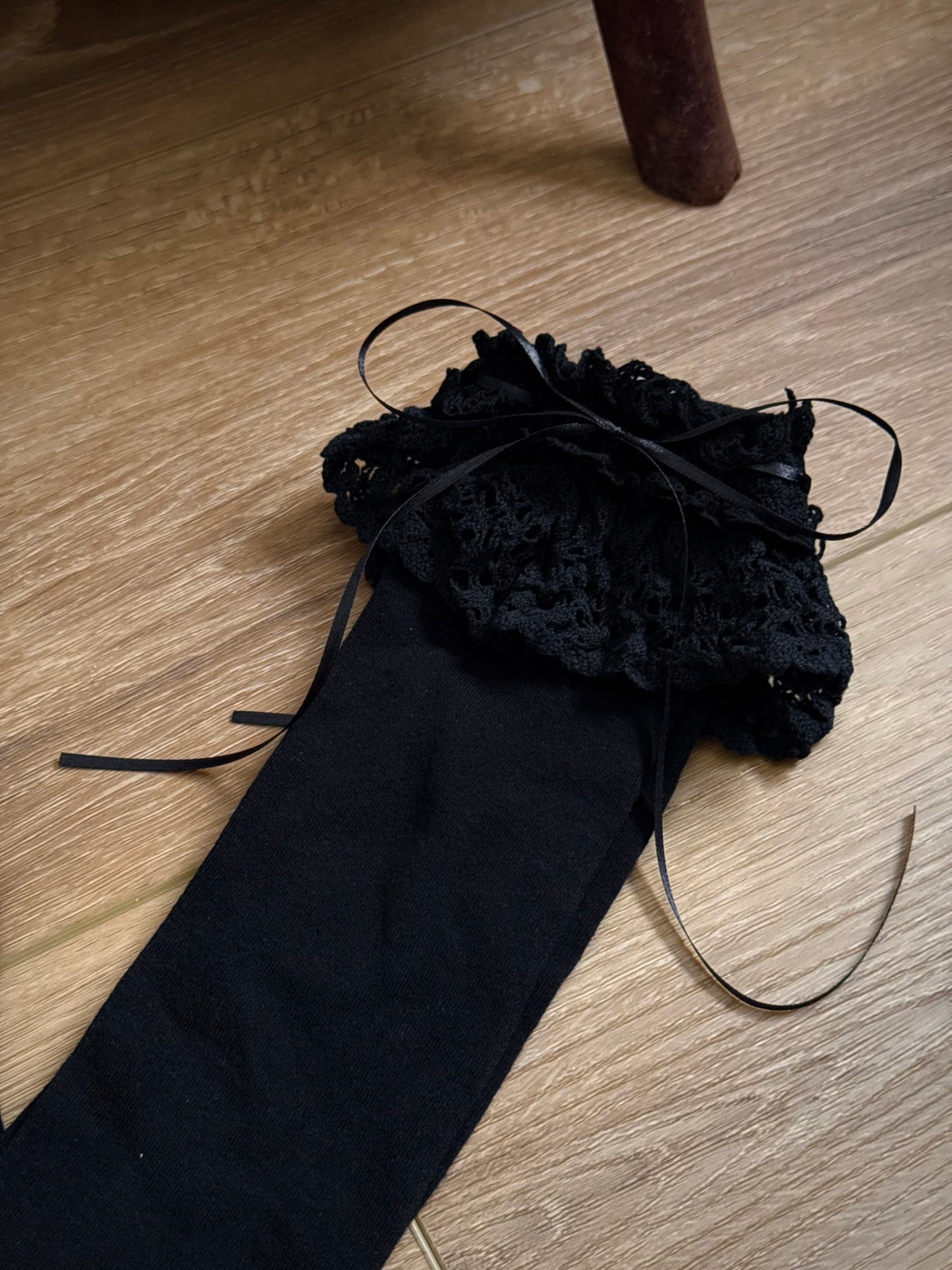 Historically Inspired Cotton Knee-High Socks with ruffled Lace Trim and ribbon ties in gothic Black on a cottagecore wooden floor.