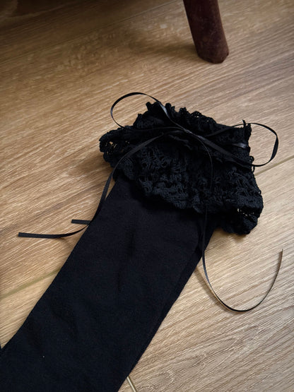 Historically Inspired Cotton Knee-High Socks with ruffled Lace Trim and ribbon ties in gothic Black on a cottagecore wooden floor.