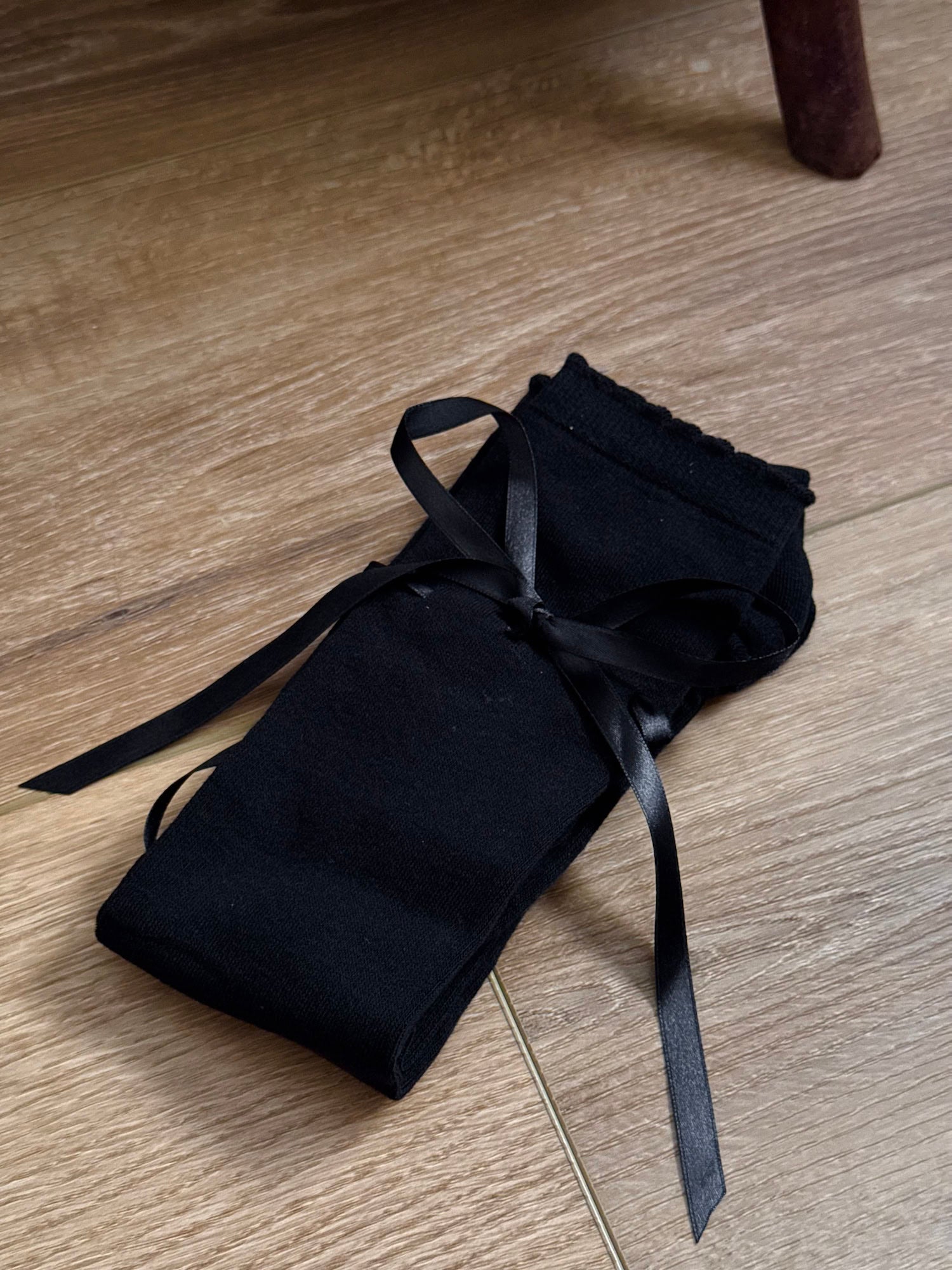 A pair of Historically Inspired Cotton Knee-High Socks with Satin Ribbon Lacing in  Gothic Black, pictured on a wooden cottage floor.