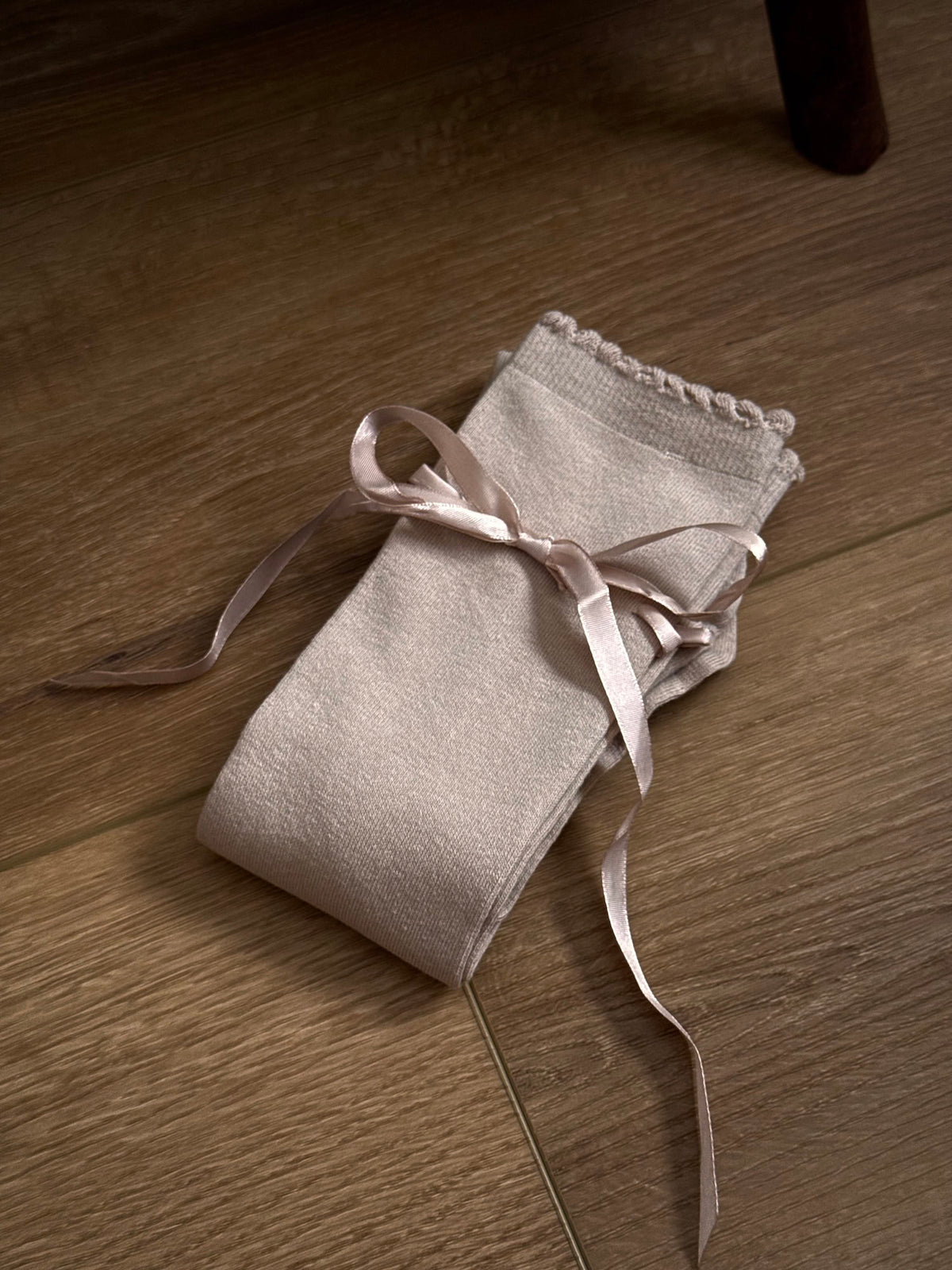 A pair of Historically Inspired Cotton Knee-High Socks with Satin Ribbon Lacing in oatmeal beige, pictured on a historic wooden cottage floor.