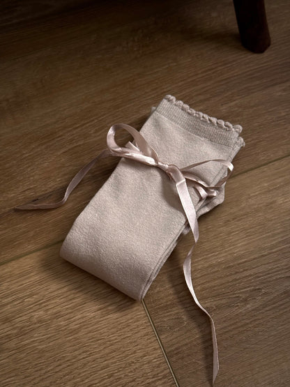 A pair of Historically Inspired Cotton Knee-High Socks with Satin Ribbon Lacing in oatmeal beige, pictured on a historic wooden cottage floor.