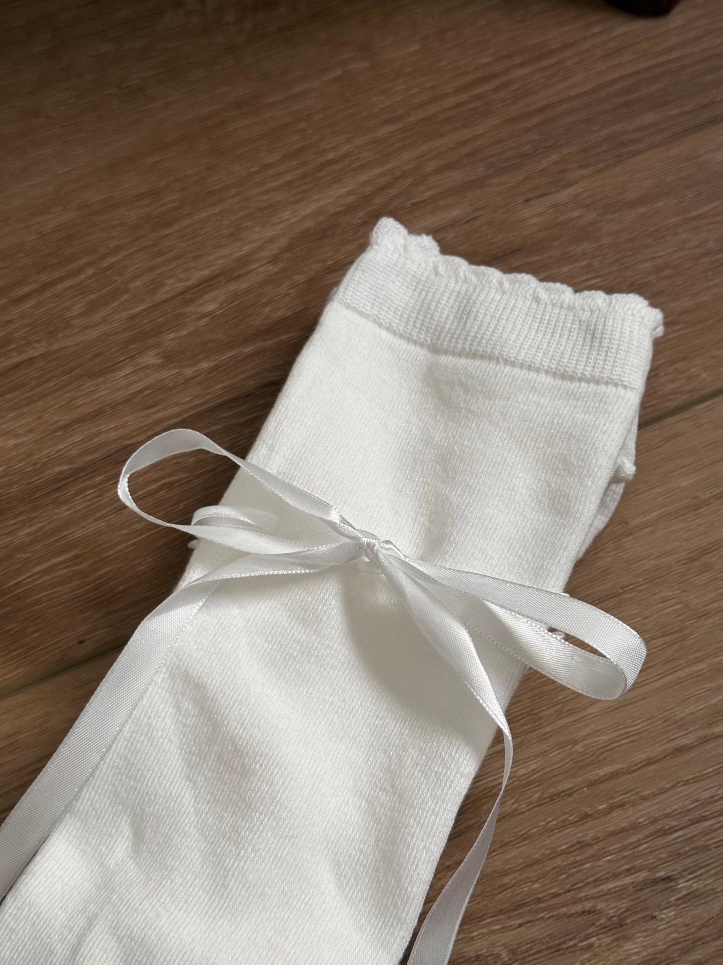 A pair of Historically Inspired Cotton Knee-High Socks with Satin Ribbon Lacing in Off-White, pictured on a historic wooden cottage floor.