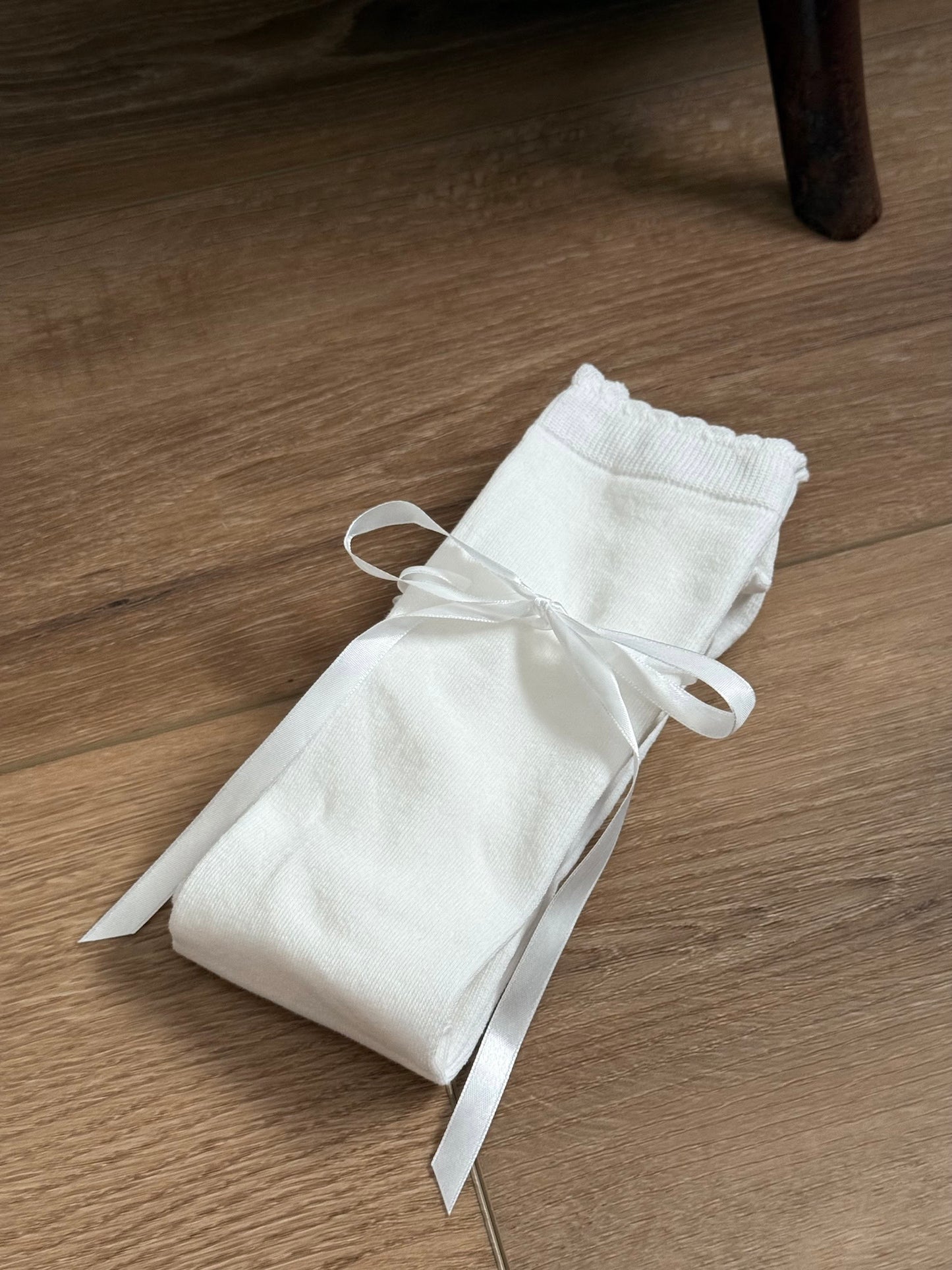 A pair of Historically Inspired Cotton Knee-High Socks with Satin Ribbon Lacing in Off-White, pictured on a historic wooden cottage floor.