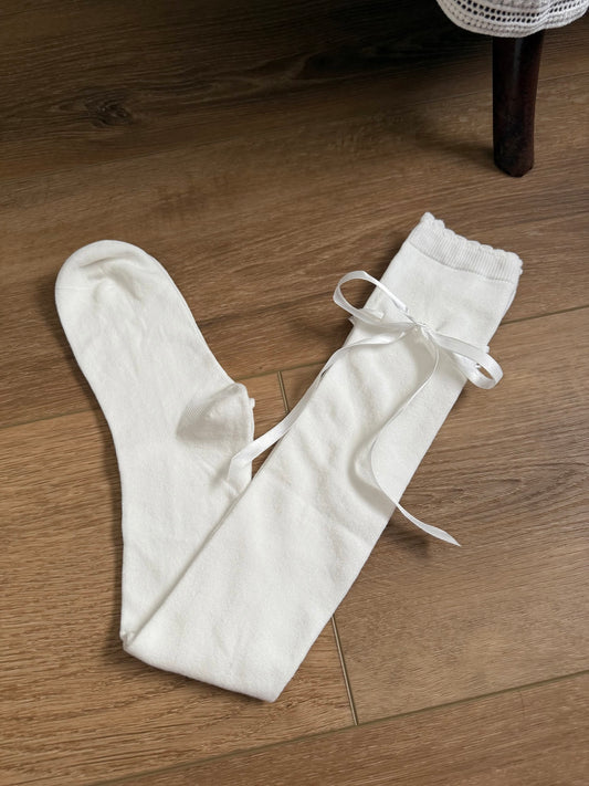A pair of Historically Inspired Cotton Knee-High Socks with Satin Ribbon Lacing in Off-White, pictured on a historic wooden cottage floor.