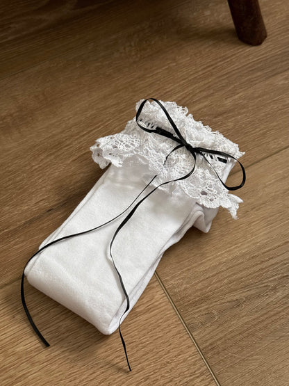 Historically Inspired white Cotton Knee-High Socks with ruffled Lace Trim and black satin ribbon ties on a cottagecore wooden floor.