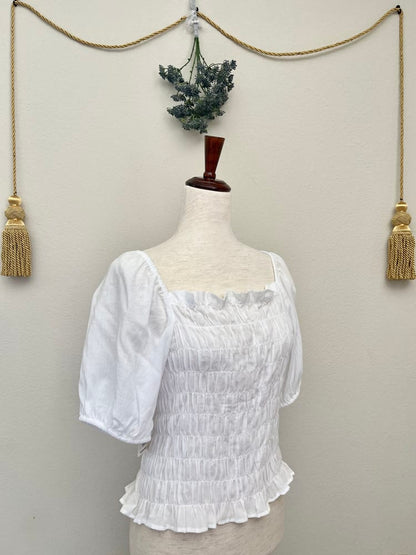 A white smocked puff sleeve historically inspired chemise blouse is pictured on a mannequin.