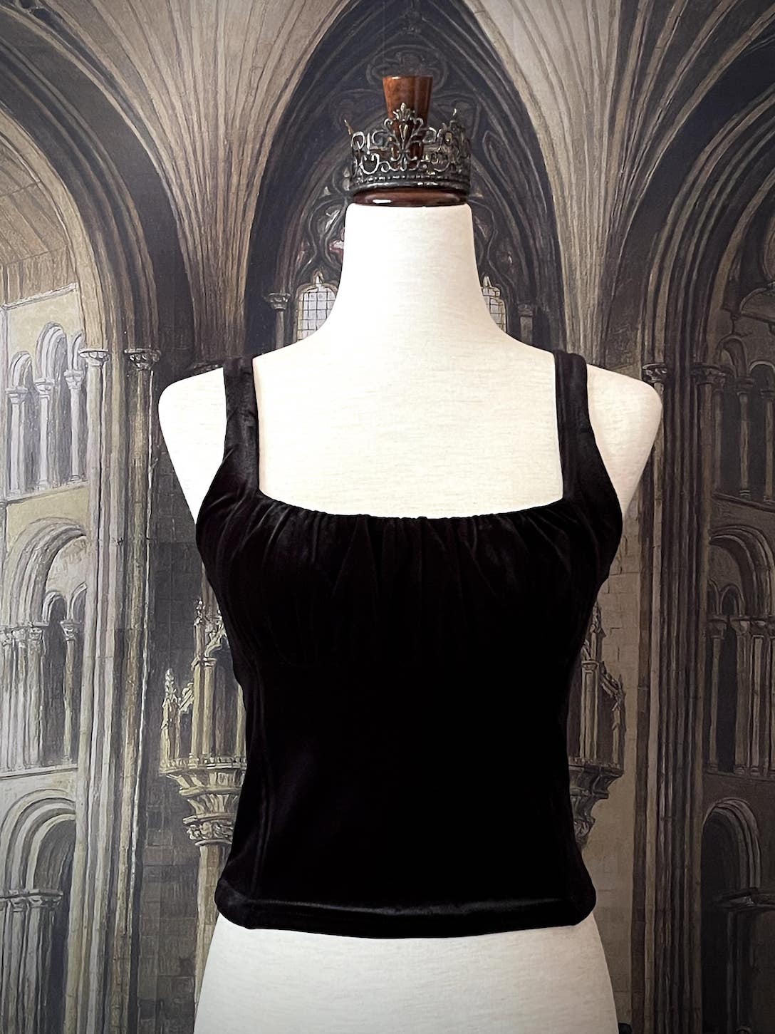 A historically inspired gothic black velvet ruched milkmaid bustier top is pictured on a mannequin in front of a gothic cathedral backdrop.