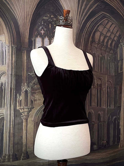 A historically inspired gothic black velvet ruched milkmaid bustier top is pictured on a mannequin in front of a gothic cathedral backdrop.