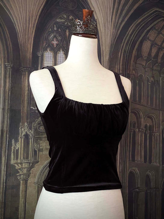 A historically inspired gothic black velvet ruched milkmaid bustier top is pictured on a mannequin in front of a gothic cathedral backdrop.