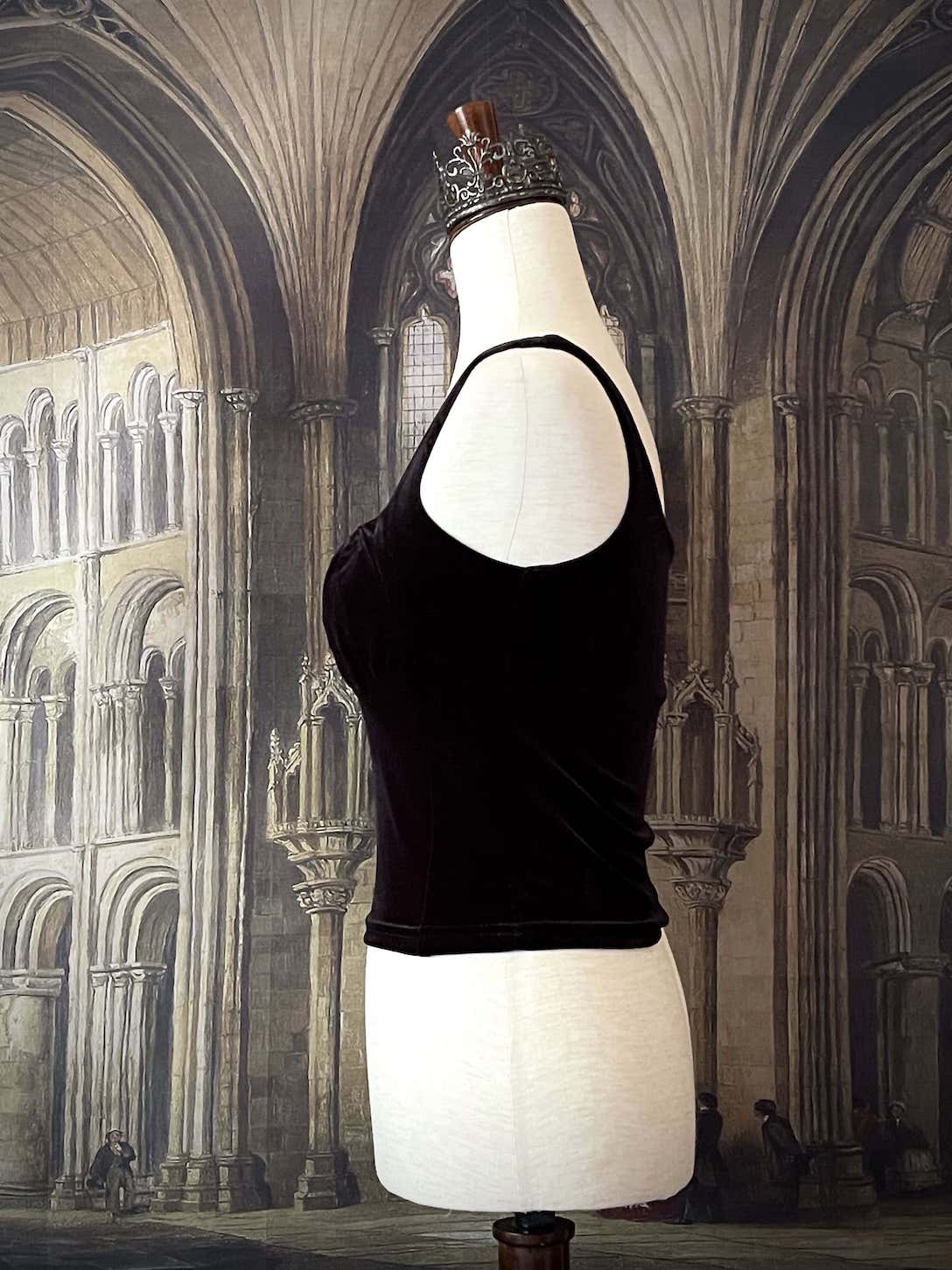 A historically inspired gothic black velvet ruched milkmaid bustier top is pictured on a mannequin in front of a gothic cathedral backdrop.