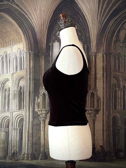 A historically inspired gothic black velvet ruched milkmaid bustier top is pictured on a mannequin in front of a gothic cathedral backdrop.