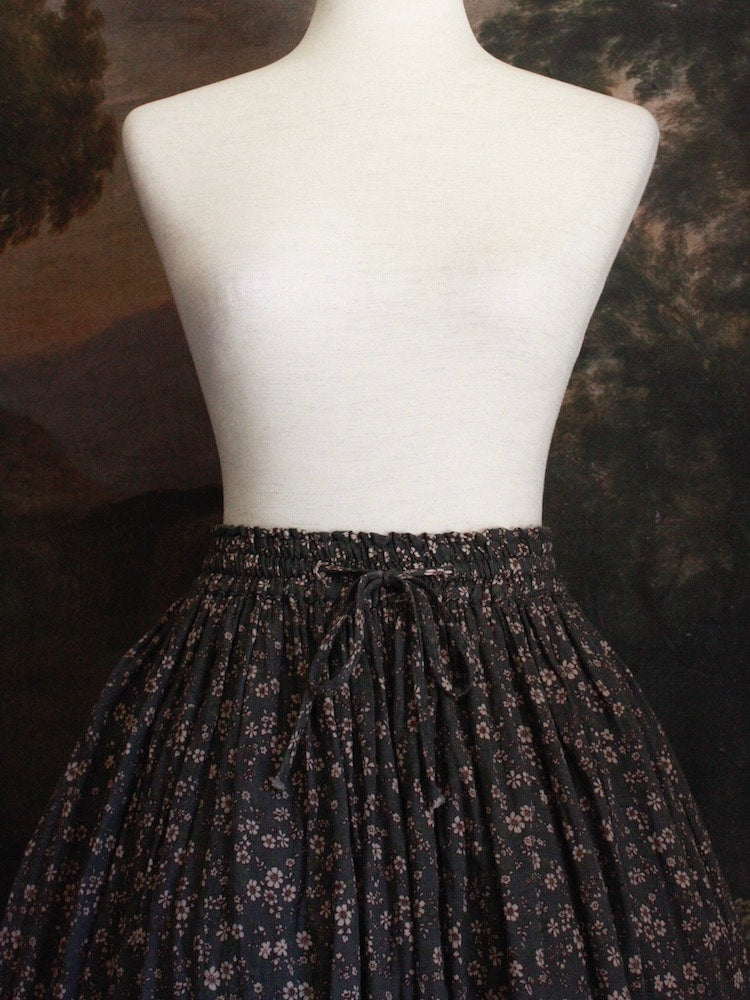 Historically Inspired victorian era peasant turn of the century  Printed Floral Cotton Maxi Skirt in Dusty Gray-Blue pictured on a mannequin in front of a classical painting. 