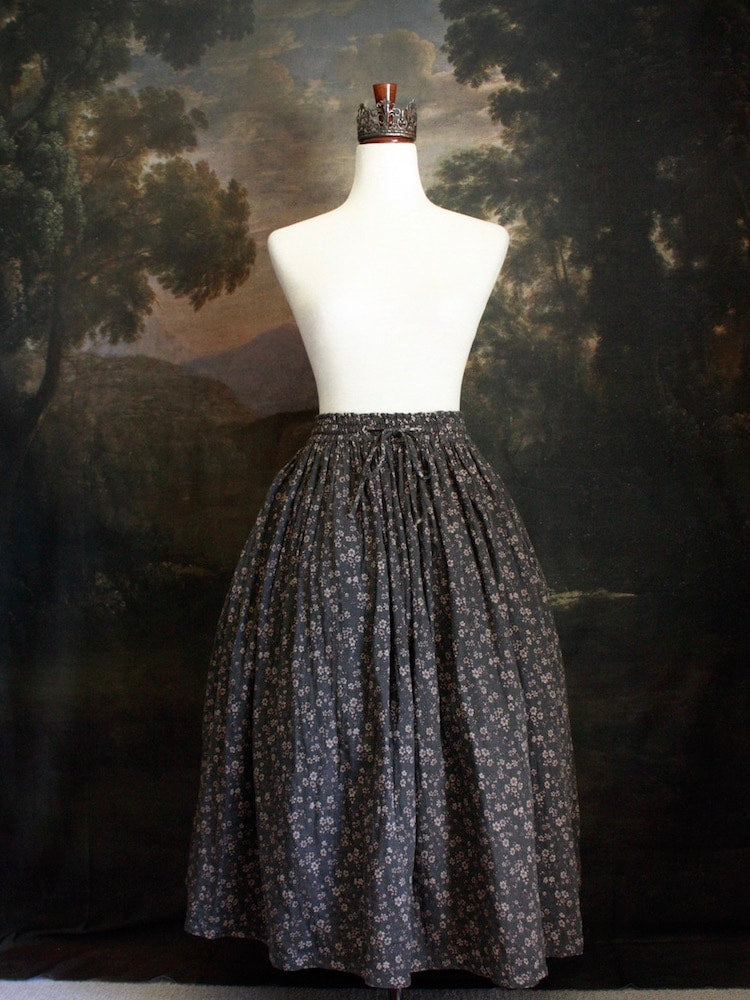 Historically Inspired victorian era peasant turn of the century  Printed Floral Cotton Maxi Skirt in Dusty Gray-Blue pictured on a mannequin in front of a classical painting. 