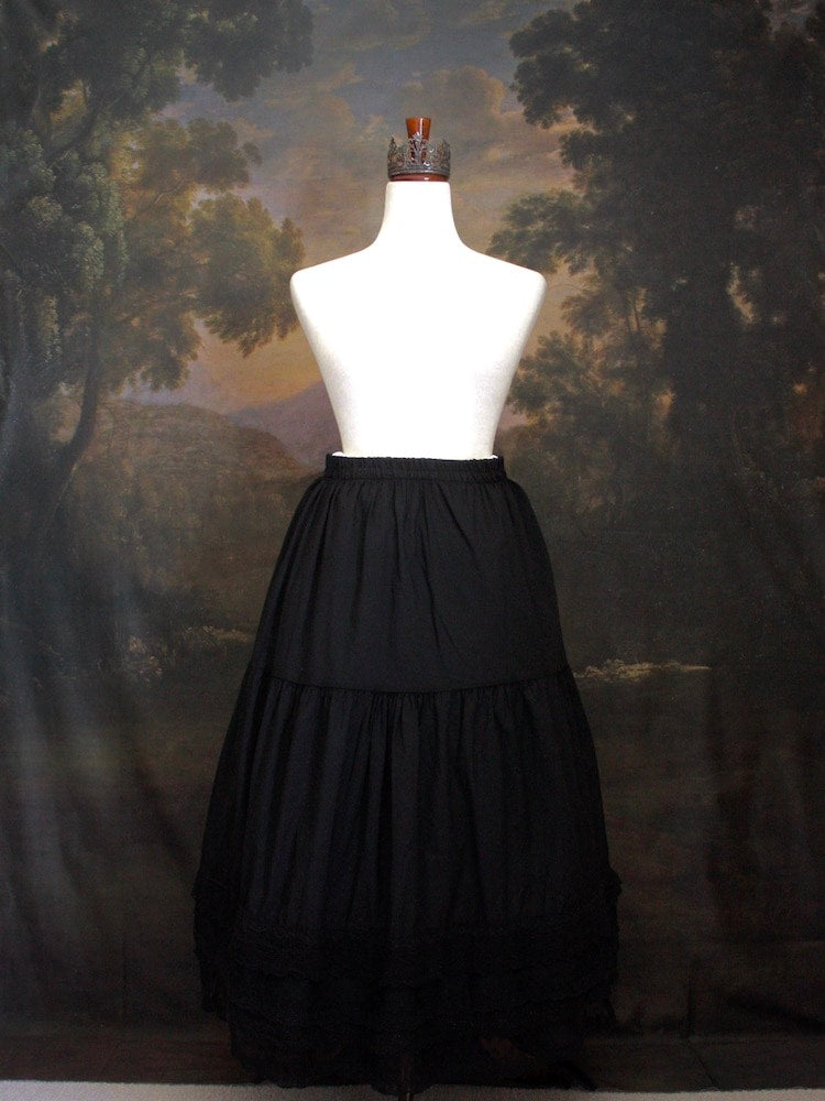 A Historically Inspired bohemian Tiered Cotton Maxi Skirt with floral Lace Trim in Black on a mannequin in front of an art history backdrop.