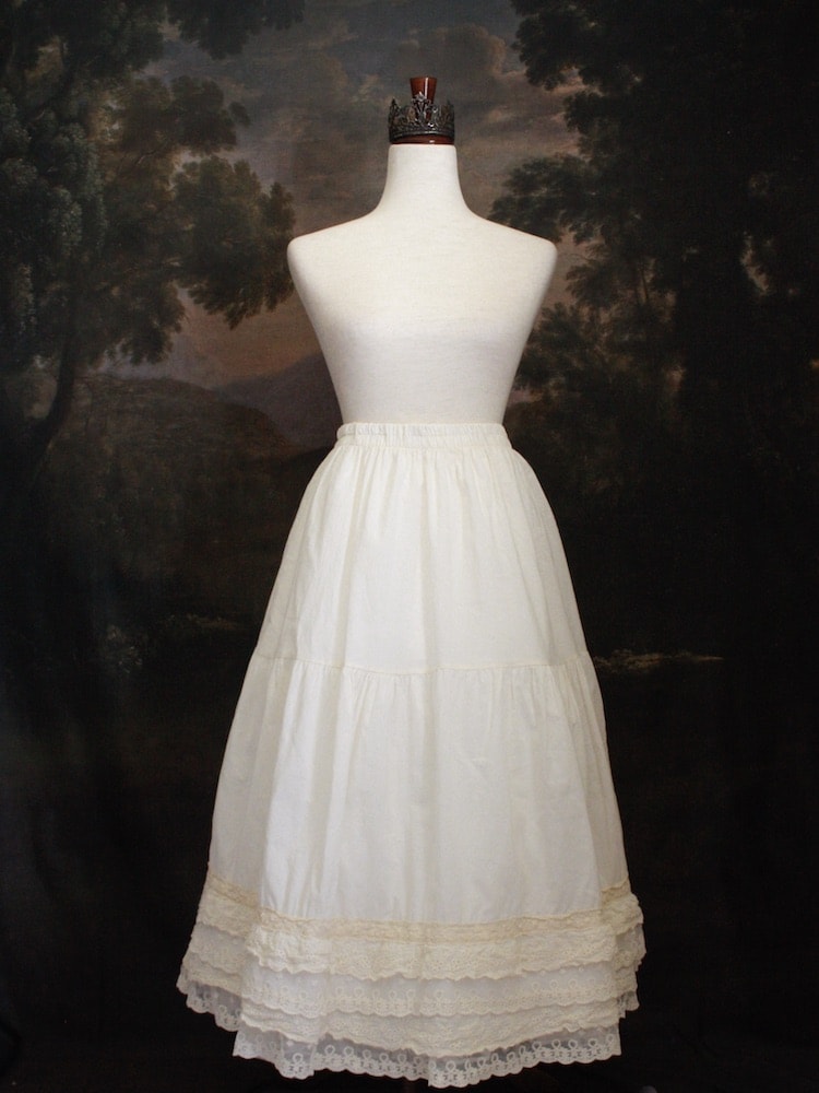 A Historically Inspired bohemian Tiered Cotton Maxi Skirt with floral Lace Trim in Ivory/Cream on a mannequin in front of an art history backdrop.