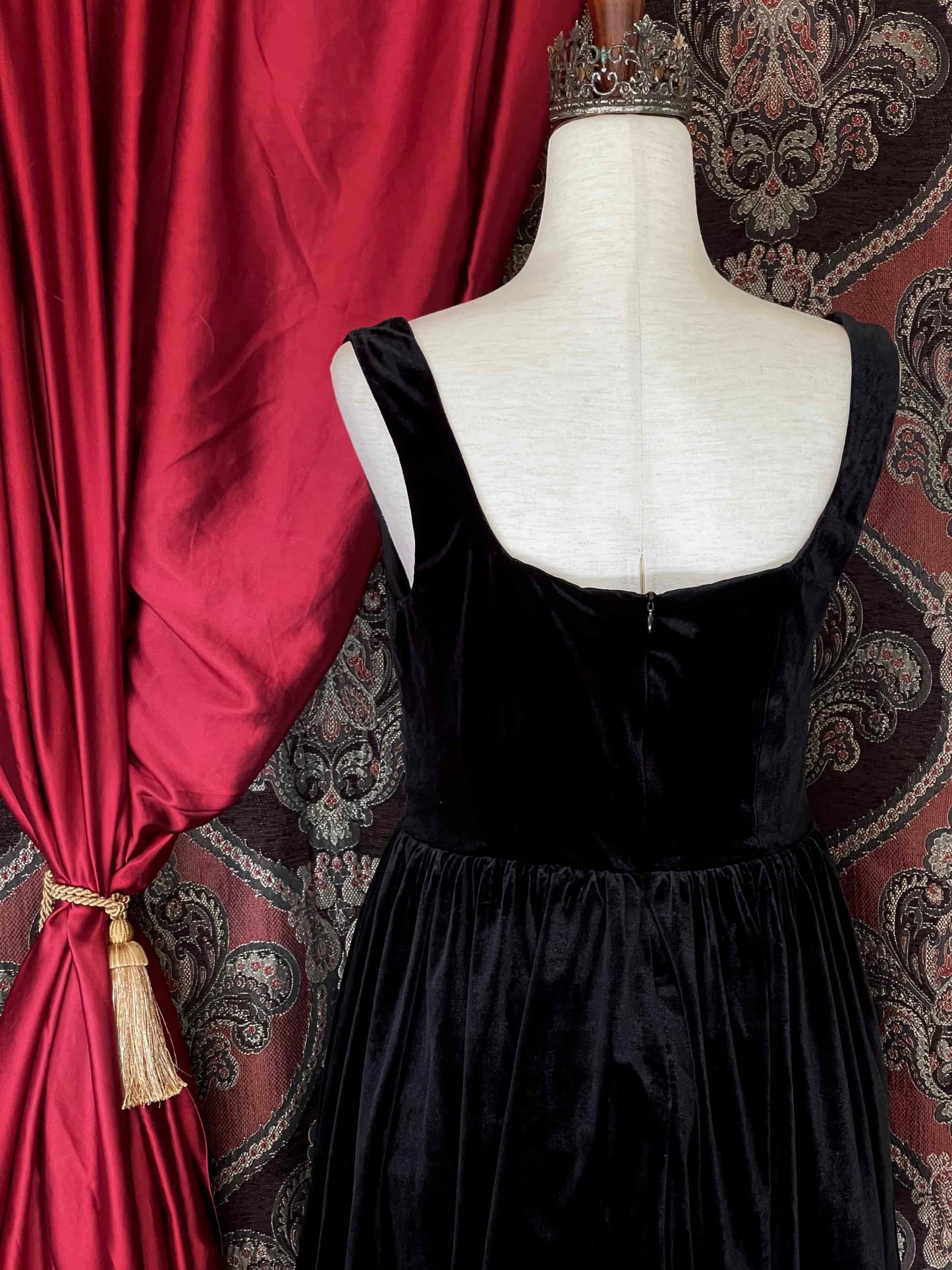 A renaissance and tudor era inspired black velvet mini dress with structured corset style bodice, pictured on a mannequin in front of a historical background.