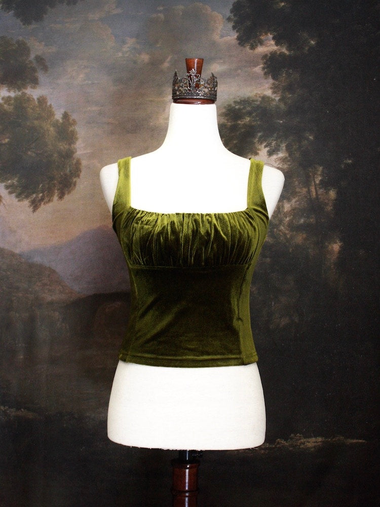 A Historically Inspired medieval fantasy Velvet Milkmaid Bustier Top in Moss Green in front of a historical painting backdrop of a forest.