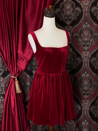 A renaissance and tudor era inspired red velvet mini dress with structured corset style bodice, pictured on a mannequin in front of a historical background.