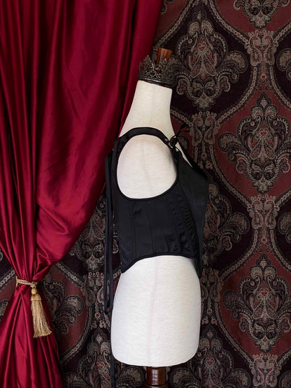 A Gothic Black Satin Renaissance Tudor Era Corset or Pair of stays is pictured on a mannequin in front of a historical Ornate Backdrop.