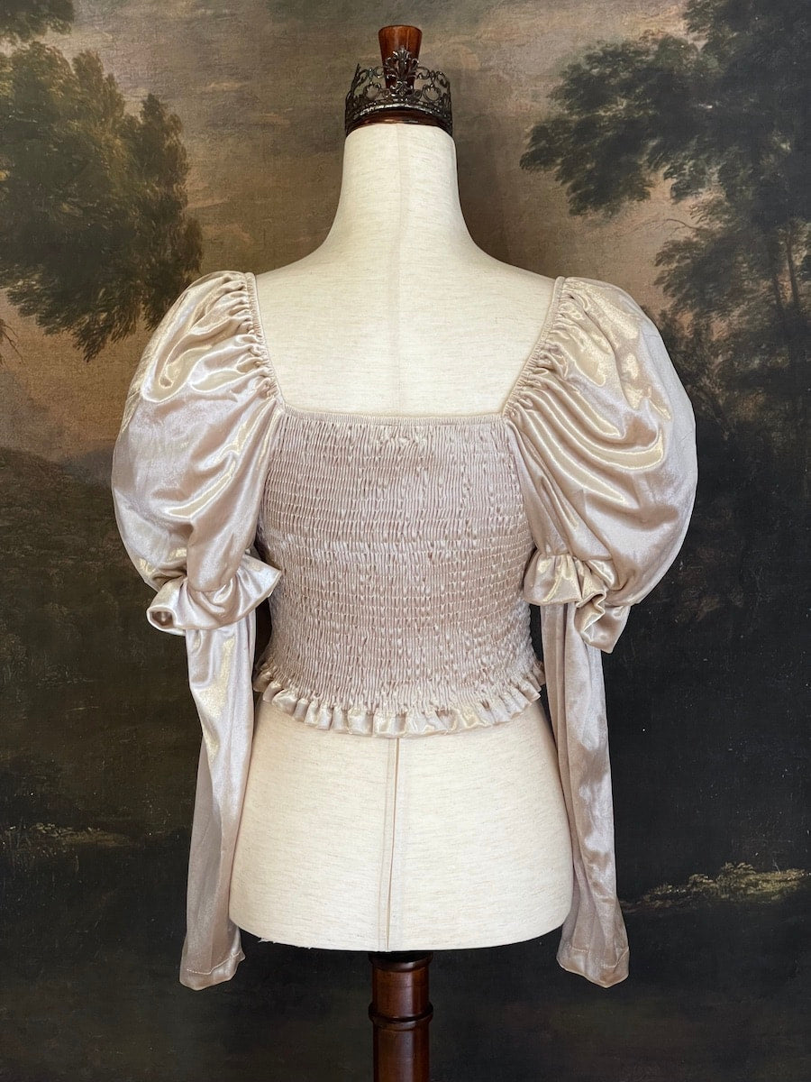 A historically Inspired champagne colored renaissance milkmaid blouse with gigot sleeves is pictured on a mannequin in front of a historical landscape painting Wallpaper.