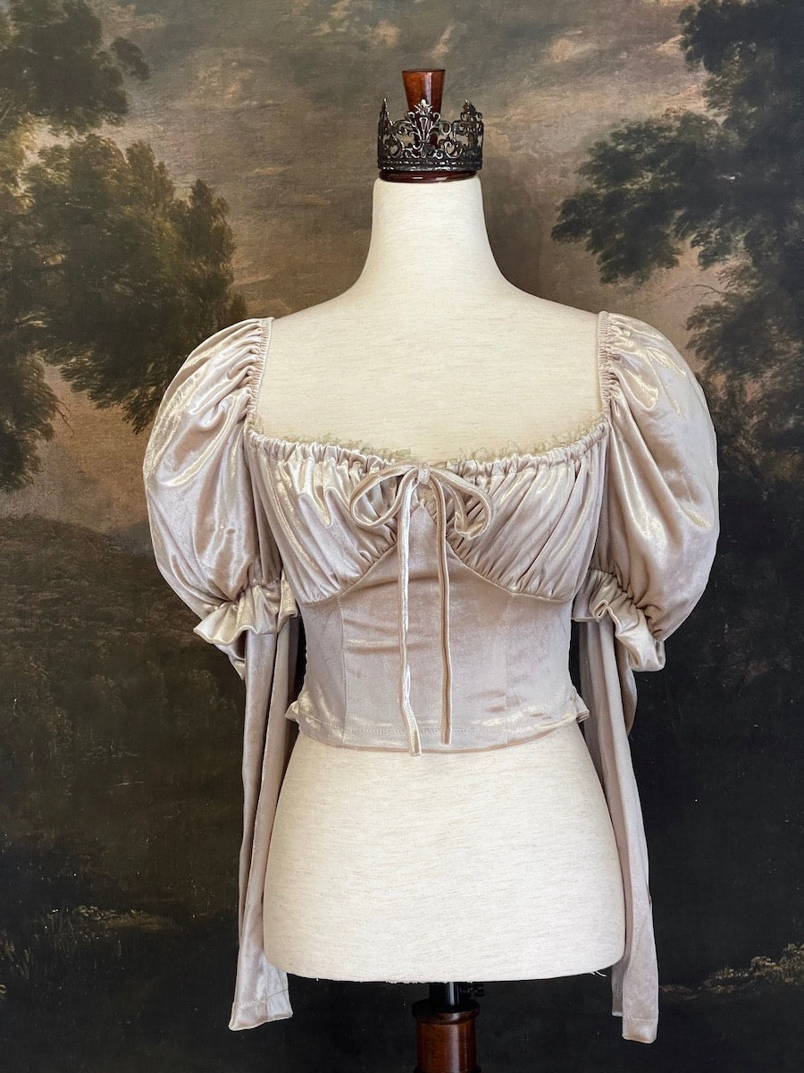 A historically Inspired champagne colored renaissance milkmaid blouse with gigot sleeves is pictured on a mannequin in front of a historical landscape painting Wallpaper.
