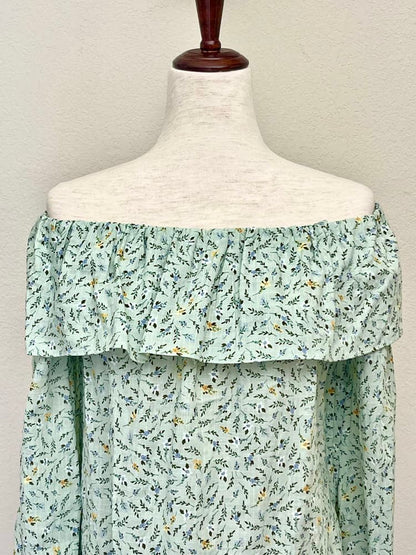 A light mint green floral print off the shoulder blouse inspired by victorian era fashion is pictured on a mannequin.