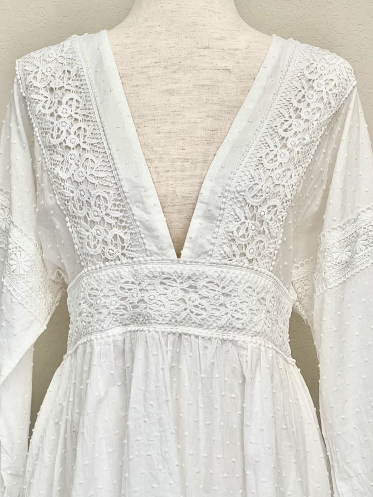 A Victorian or Edwardian inspired white cotton vneck bishop sleeve open back dress with crocheted lace details is pictured on a mannequin.