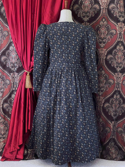 A vintage Laura Ashley historically inspired floral print corduroy prairie dress gown with puff sleeves and a square neckline is pictured in front of an ornate backdrop.