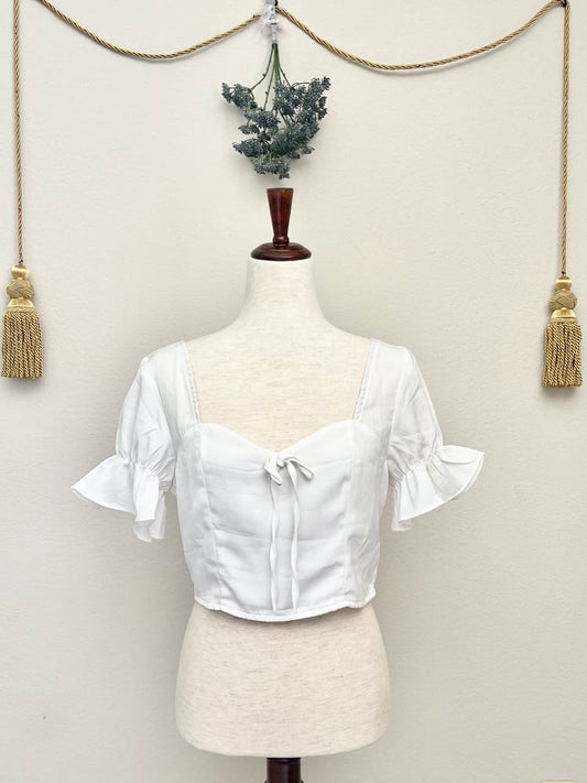 A white edwardian era inspired cropped blouse with ruffle sleeves is pictured on a mannequin in front of a classical background.