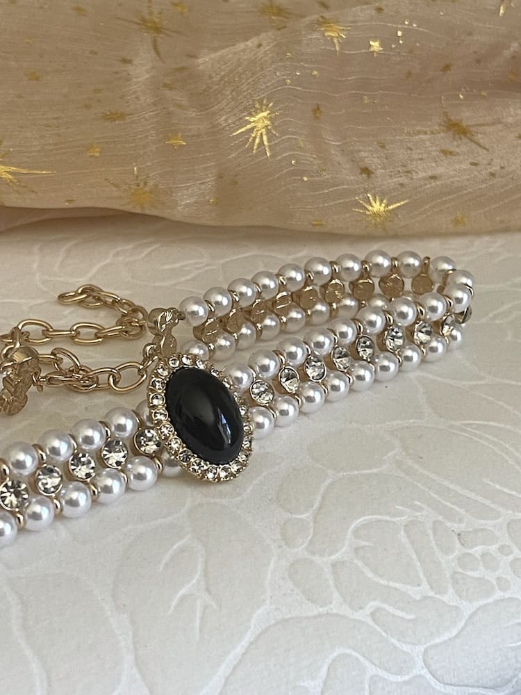 A Historically inspired renaissance tudor baroque rococo regency victorian edwardian pearl beaded crystal accent choker necklace in black is pictured on a floral puff.